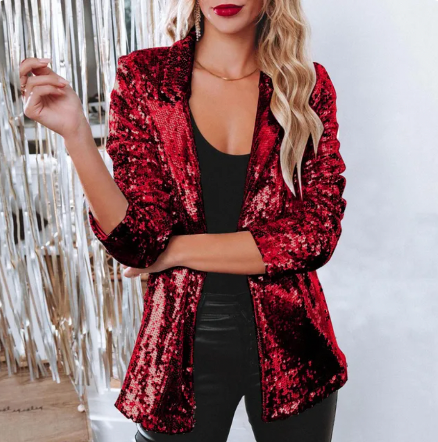 Frau in rotem Paillettenblazer, schwarzem Top und Lederhose, steht vor silbernem Hintergrund. Elegante Mode, glamouröser Look, Abendgarderobe.