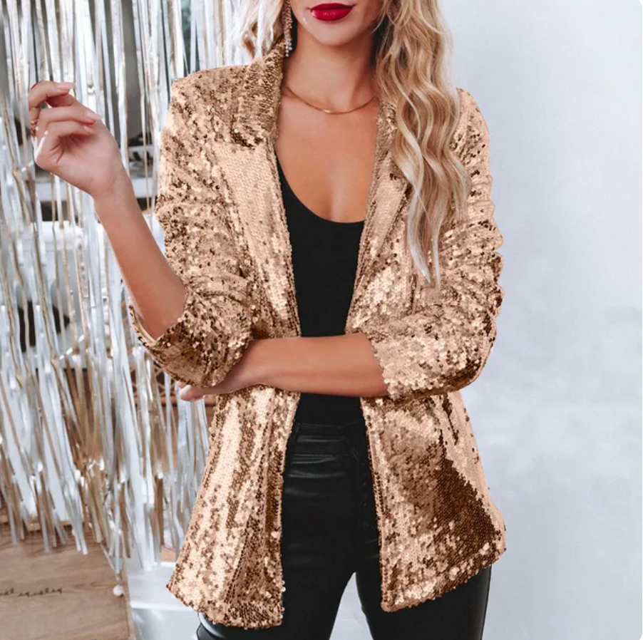 Blonde Frau in goldenem Paillettenblazer, schwarzem Top und Lederhose vor silbernem Hintergrund. Elegante Mode, glamouröser Look.