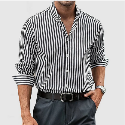 Mann in gestreiftem Hemd, schwarz-weiß, mit hochgekrempelten Ärmeln, trägt schwarze Hose und Uhr. Elegante Herrenmode, Business-Look.