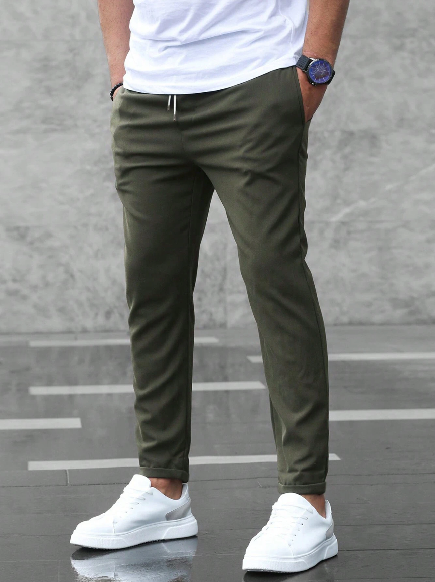 Mann in olivgrüner Jogginghose, weißem T-Shirt und weißen Sneakers. Lässiger Streetwear-Look, ideal für Freizeit und Sport.
