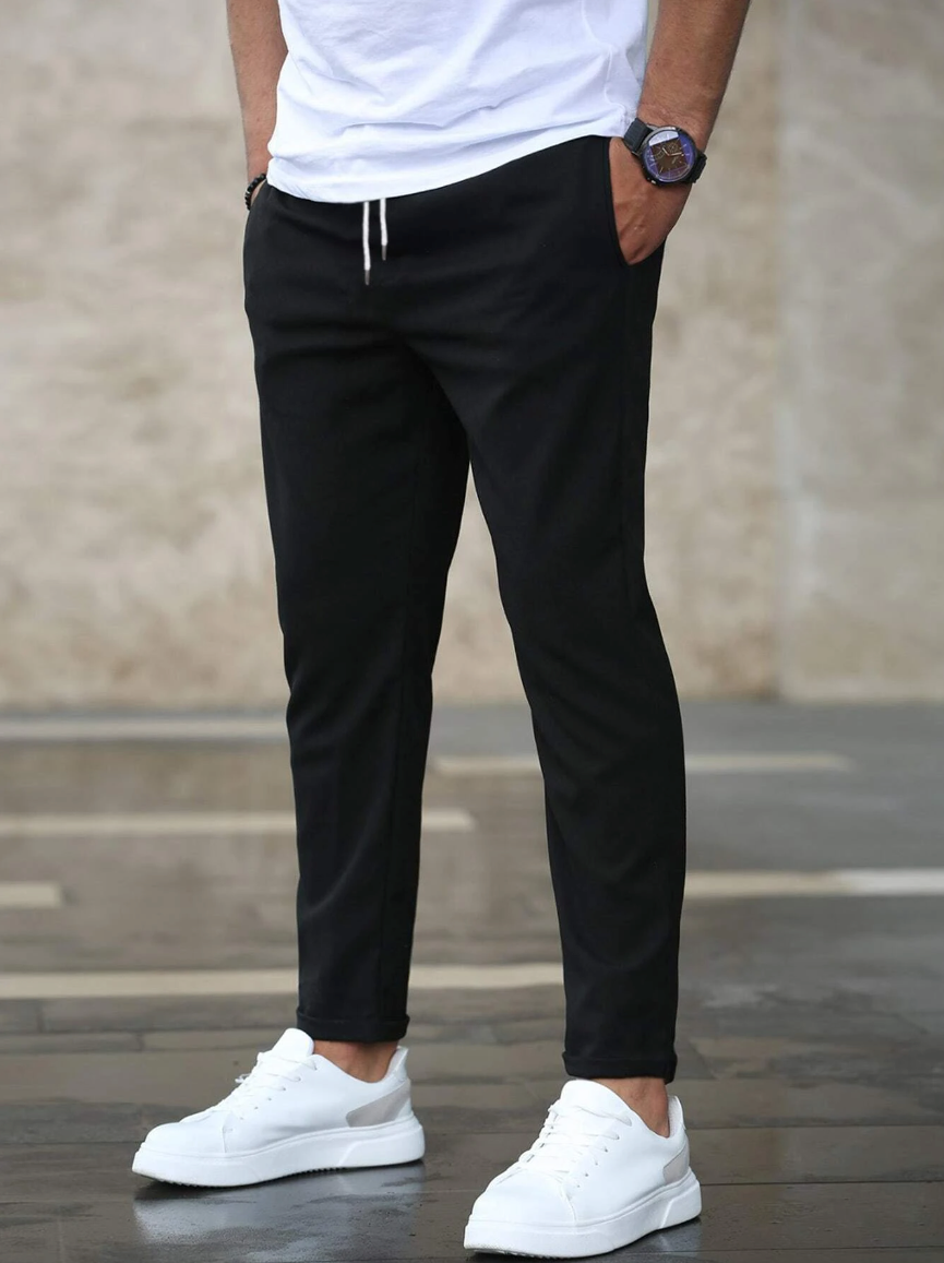 Mann in schwarzer Jogginghose und weißen Sneakers, lässiger Stil, moderne Herrenmode, urbaner Hintergrund, Freizeitlook, Modeaccessoires.