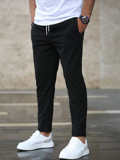 Mann in schwarzer Jogginghose und weißen Sneakers, lässiger Stil, moderne Herrenmode, urbaner Hintergrund, Freizeitlook, Modeaccessoires.