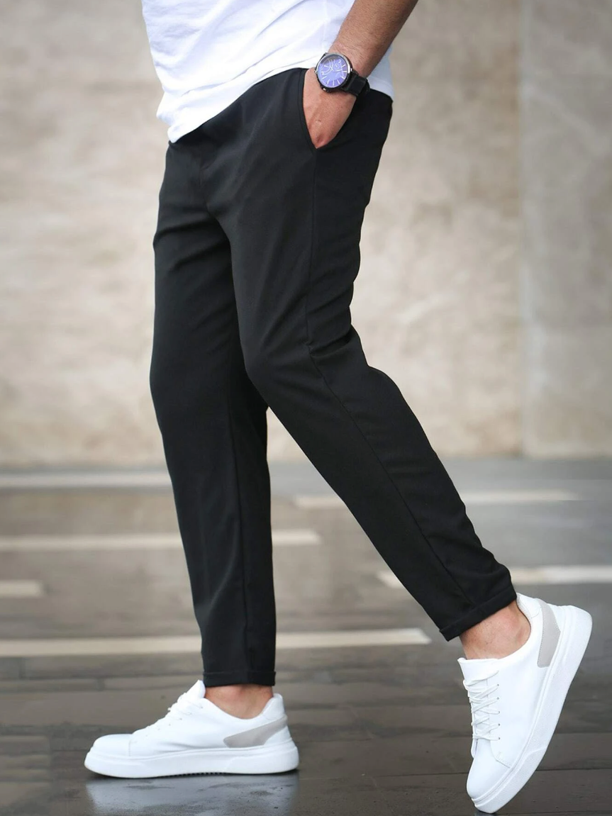 Mann in schwarzer Hose und weißen Sneakers, seitlich gehend. Moderne Herrenmode, lässiger Stil, urbane Kleidung, stilvolle Freizeitbekleidung.