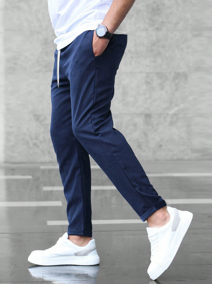 Mann in blauer Jogginghose und weißen Sneakers, seitlich gehend. Moderne Freizeitmode, sportlicher Look, grauer Hintergrund.