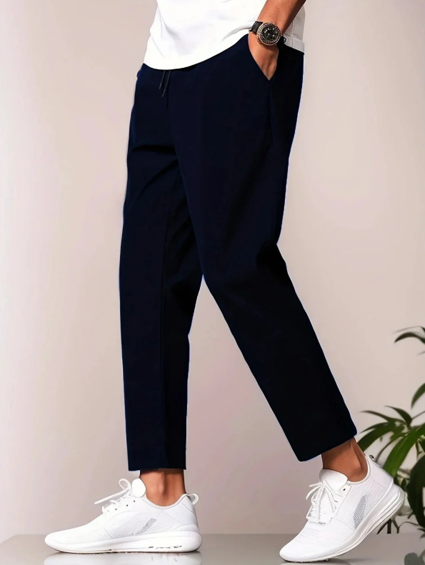 Mann trägt dunkelblaue Chinohose und weiße Sneaker, seitliche Ansicht. Moderne Herrenmode, lässiger Stil, elegante Freizeitkleidung.