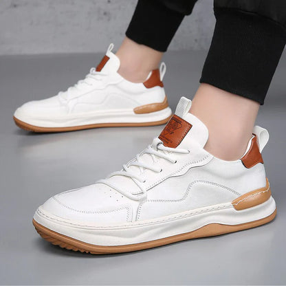 Weiße Sneaker mit braunen Akzenten, Gummisohle und Schnürsenkeln auf grauem Hintergrund. Modische Herrenschuhe, ideal für Freizeit und Sport.