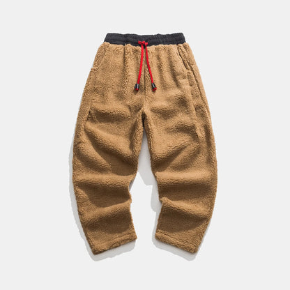 Braune Fleece-Jogginghose mit elastischem Bund und rotem Kordelzug auf weißem Hintergrund. Bequeme, warme Herrenmode für Herbst und Winter.