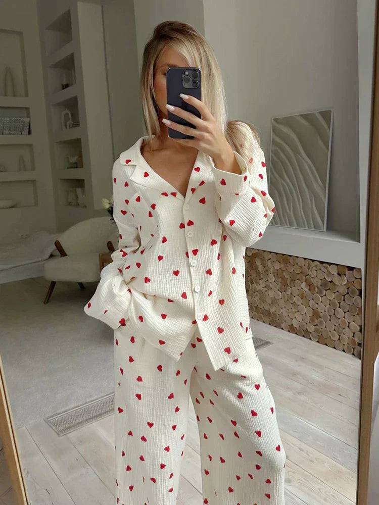 Frau in weißem Pyjama mit roten Herzen, macht Selfie im modernen Schlafzimmer. Bequeme Nachtwäsche, stilvolles Design, gemütliche Atmosphäre.