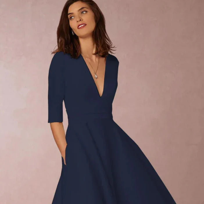 Frau in elegantem, dunkelblauem Kleid mit V-Ausschnitt und halblangen Ärmeln vor neutralem Hintergrund. Perfekt für Abendmode und elegante Anlässe.