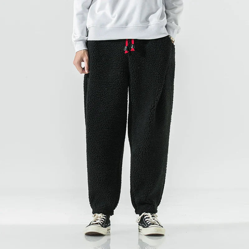 Schwarze Fleece-Jogginghose für Herren, lässiger Stil, kombiniert mit weißen Sneakers und grauem Sweatshirt. Bequem und modisch für den Alltag.