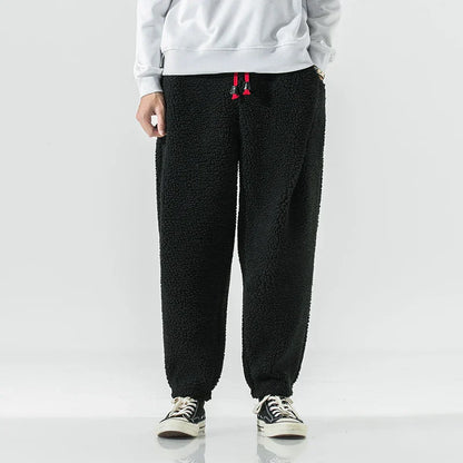 Schwarze Fleece-Jogginghose für Herren, lässiger Stil, kombiniert mit weißen Sneakers und grauem Sweatshirt. Bequem und modisch für den Alltag.