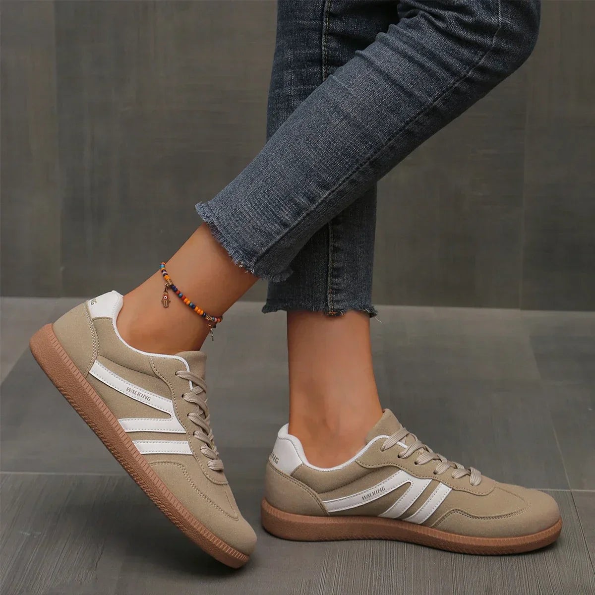 Damen Sneaker in Beige mit weißen Streifen, kombiniert mit blauen Jeans. Modischer Freizeitschuh, ideal für urbanen Stil und Komfort.
