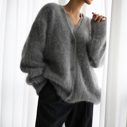 Frau trägt grauen, flauschigen Mohair-Cardigan mit V-Ausschnitt und Knöpfen, kombiniert mit schwarzer Hose. Elegante, gemütliche Herbstmode.