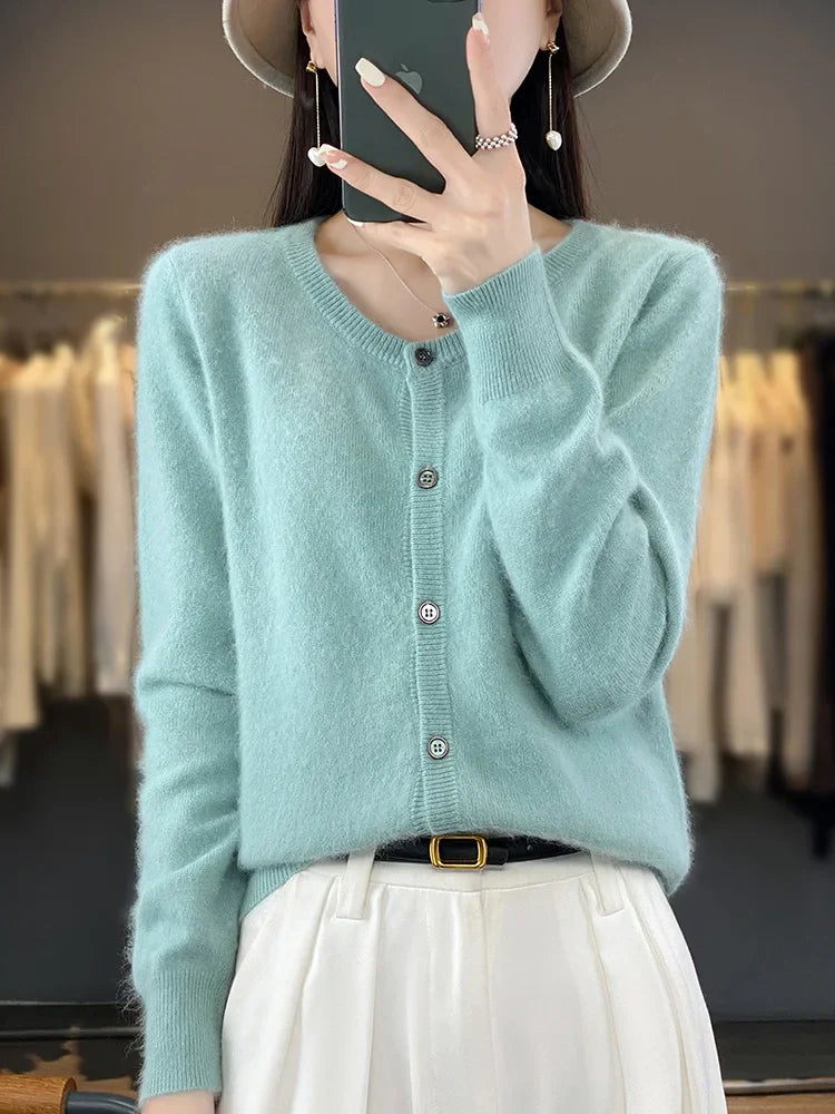 Frau in hellblauem Strickcardigan und weißer Hose, hält Smartphone, modisches Outfit, Herbstmode, eleganter Look, Shopping, Damenbekleidung.