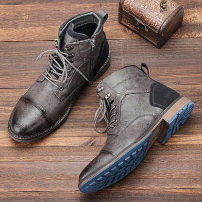 Graue Herrenstiefel aus Leder mit blauer Sohle auf Holzboden, neben einer kleinen, verzierten Truhe. Robuste Winterstiefel, modisch und funktional.