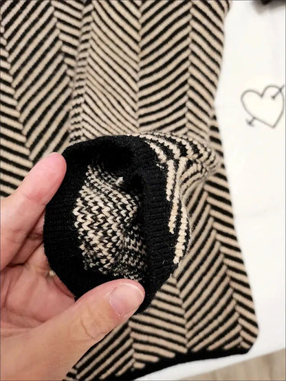 Nahaufnahme eines schwarz-beige gestreiften Strickpullovers mit Zickzackmuster, gehalten von einer Hand. Modetrend, Strickmode, Herbstbekleidung.