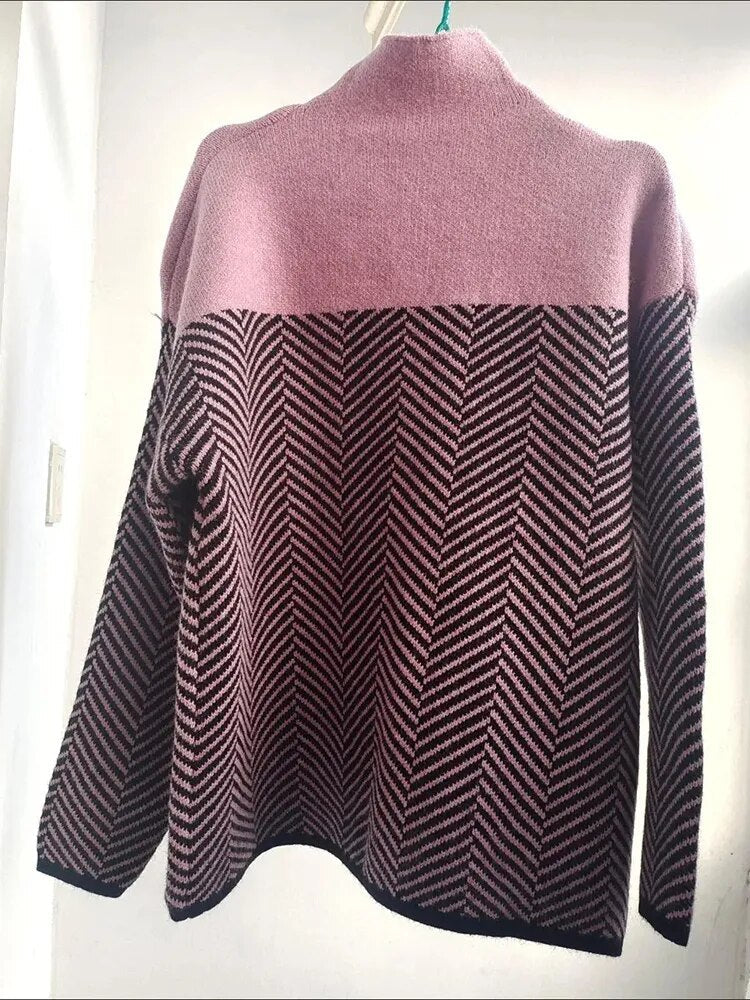 Rosa und schwarzer Strickpullover mit Zickzackmuster, hängend an einem Kleiderbügel. Modischer Damenpullover, warm und stilvoll.