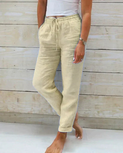 Damen Leinenhose beige, lässig, mit Kordelzug, Taschen, knöchellang, ideal für Sommermode, bequem und stilvoll, vor Holzwand.