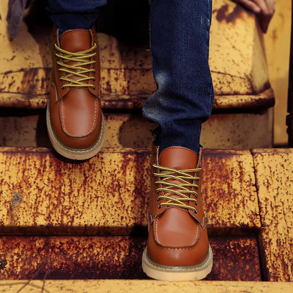 Braune Lederstiefel mit gelben Schnürsenkeln auf rostiger Metalltreppe, getragen von Person in blauer Jeans. Outdoor-Mode, robuste Schuhe.