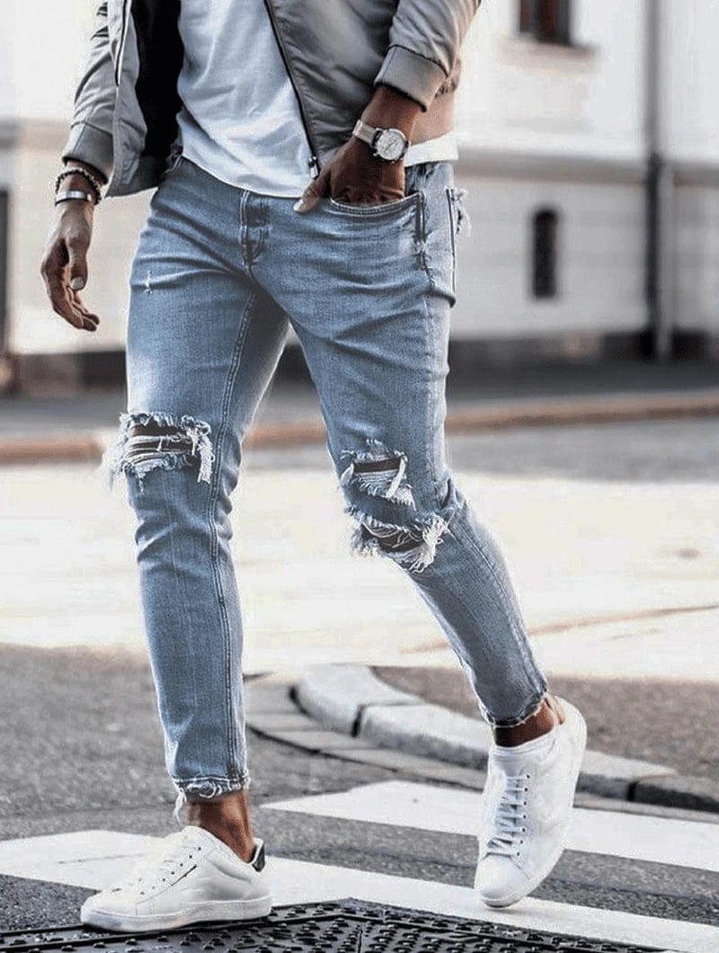 Mann in zerrissenen Jeans und weißen Sneakers überquert Straße. Modetrend, lässiger Stil, urbane Mode, Herrenbekleidung, Streetwear.