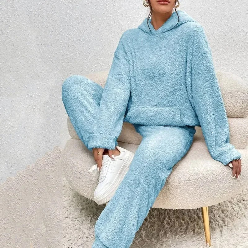 Frau in hellblauem Fleece-Hoodie und Jogginghose sitzt auf einem Stuhl, trägt weiße Sneaker. Bequeme Damenmode, Freizeitkleidung, Winteroutfit.
