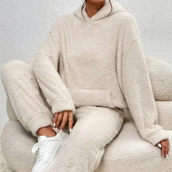 Frau in beigem, flauschigem Hoodie und Jogginghose sitzt auf einem Sessel. Bequeme Loungewear, gemütlicher Look, modische Freizeitkleidung.