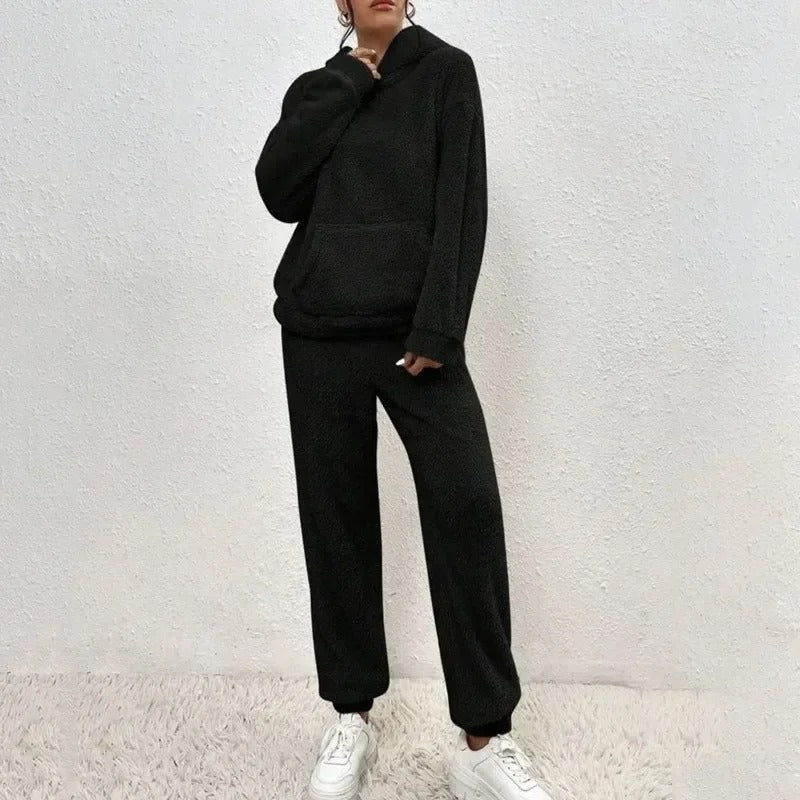 Dunkler Fleece-Trainingsanzug für Damen, bestehend aus Hoodie und Jogginghose, kombiniert mit weißen Sneakers. Bequemes Freizeitoutfit.