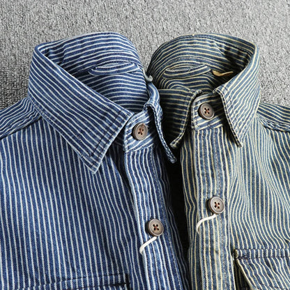 Zwei gestreifte Hemden aus Denim-Stoff, blau und grün, mit Holzknöpfen auf grauem Hintergrund. Modische Herrenbekleidung, lässiger Stil.