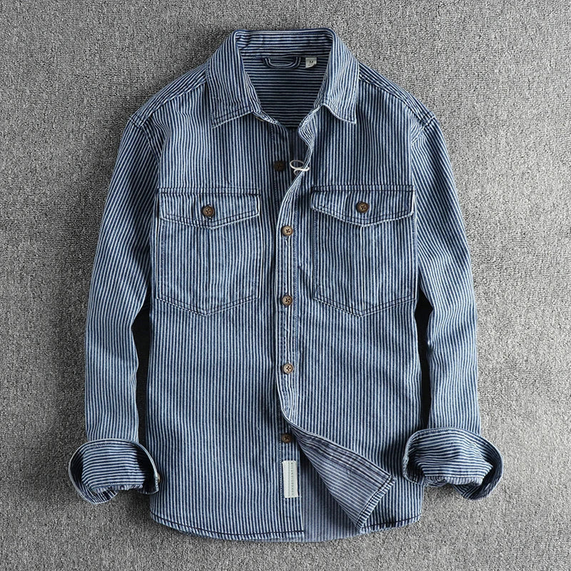Gestreiftes Jeanshemd mit langen Ärmeln, zwei Brusttaschen und Knopfleiste, auf grauem Hintergrund. Modisches Herrenhemd, lässiger Stil.