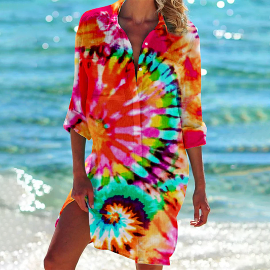 Frau am Strand in buntem Batik-Kleid, leuchtende Farben, Sommermode, Meereshintergrund, Freizeitkleidung, Strandoutfit, modischer Look.