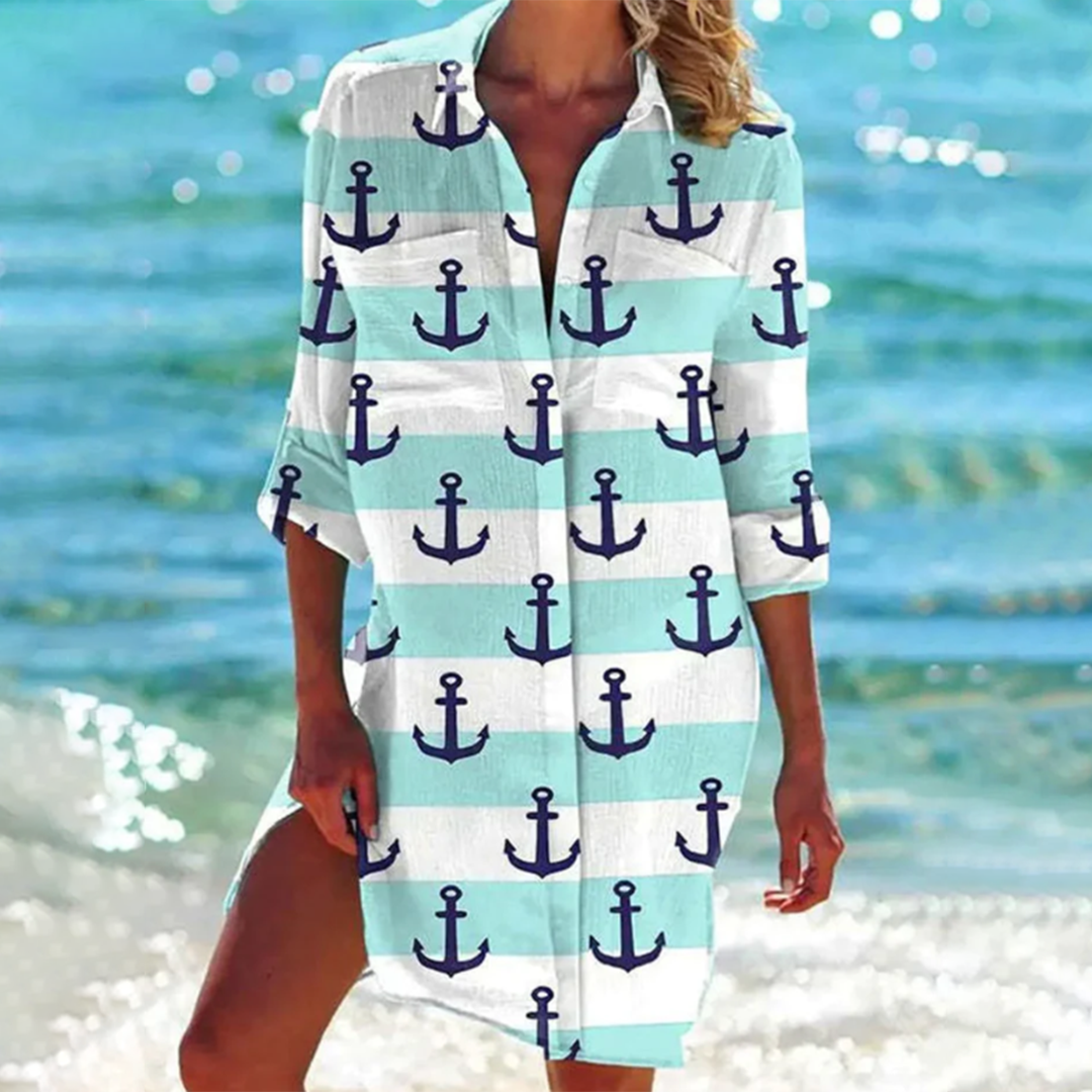 Frau am Strand in einem maritimen Strandkleid mit Anker-Muster, türkis-weiß gestreift. Sommermode, Strandoutfit, maritimer Stil.