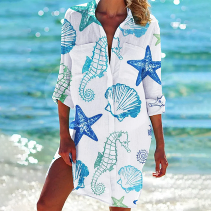 Frau am Strand in weißem Strandkleid mit blauen Seesternen, Seepferdchen und Muscheln. Sommermode, Strandkleidung, maritimes Design.