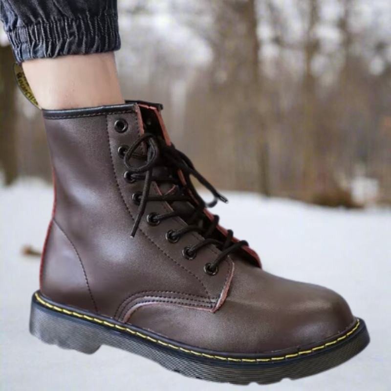 Brauner Lederstiefel mit gelber Naht auf schneebedecktem Waldweg. Modischer Winterstiefel, robust und wetterfest. Outdoor-Boots für kalte Tage.