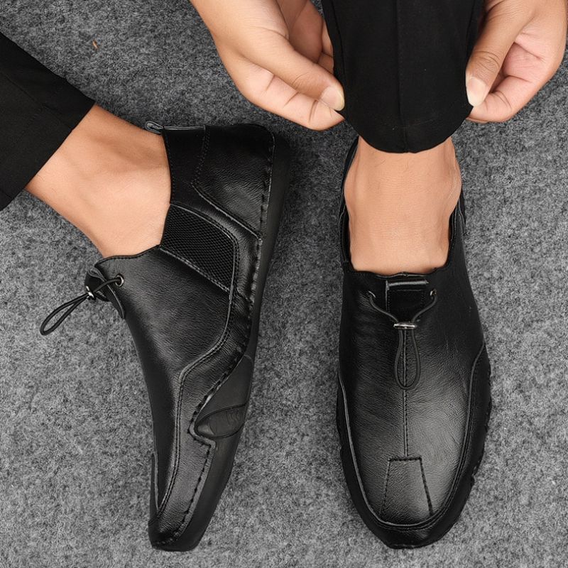 Schwarze Herren-Lederslipper, elegant und modern, auf grauem Teppich. Bequeme Freizeitschuhe, ideal für Büro oder Alltag.