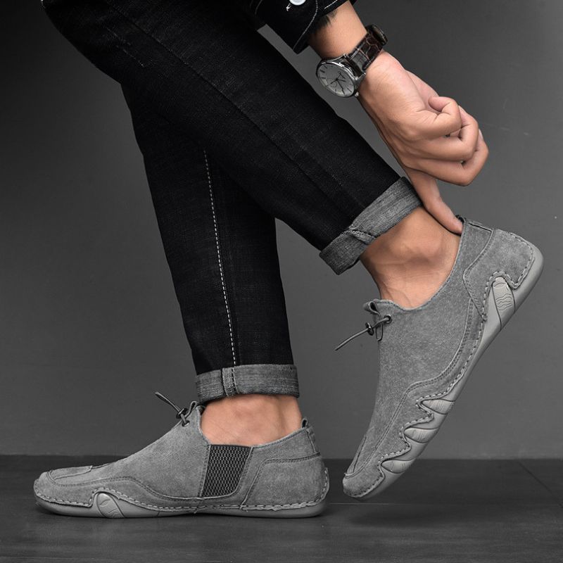 Graue Herren-Slipper aus Wildleder, getragen mit schwarzer Jeans. Bequeme Freizeitschuhe, ideal für stilvolle, lässige Outfits.