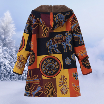 Bunter Wintermantel mit ethnischen Mustern, Kapuze und warmem Futter vor schneebedeckter Landschaft. Ideal für kalte Wintertage.