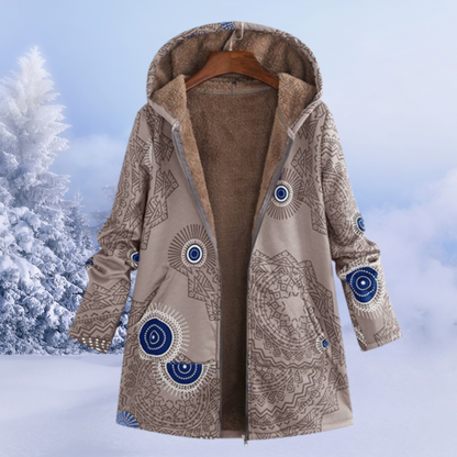Damen Wintermantel mit Kapuze, geometrischem Muster und Fleece-Futter, beige-blau, vor verschneiter Landschaft. Warm, stilvoll, wintertauglich.