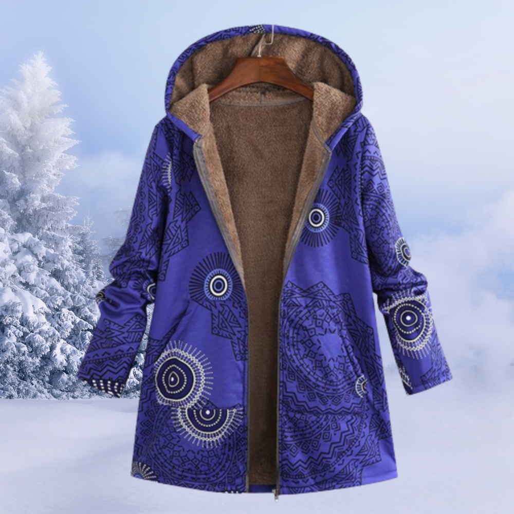 Blauer Damen-Wintermantel mit Kapuze, ethnischem Muster und Fleece-Futter, hängend vor verschneiter Winterlandschaft. Warm, stilvoll, bequem.