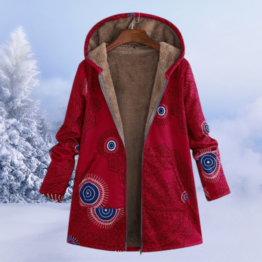 Roter Damen-Wintermantel mit Kapuze, ethnischem Muster und Fleece-Futter, hängend vor verschneiter Winterlandschaft. Warm, stilvoll, bequem.