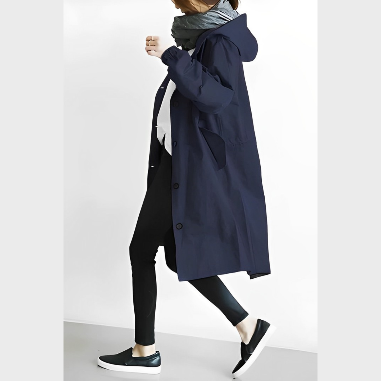 Frau in dunkelblauem Mantel, schwarzer Leggings und Sneakers, geht seitlich. Modischer Herbstlook, lässiger Stil, bequeme Kleidung.