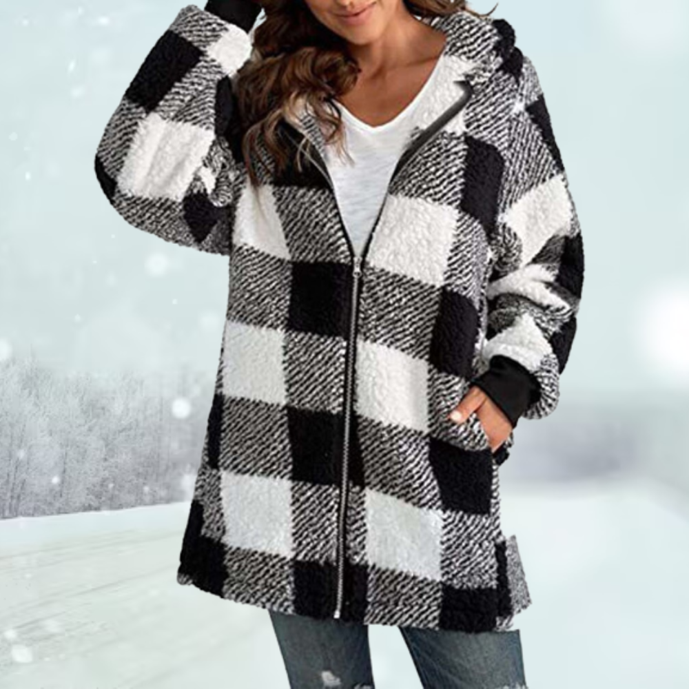 Frau in kariertem Wintermantel, schwarz-weiß, mit Kapuze, vor schneebedeckter Landschaft. Modetrend, warme Damenbekleidung, Wintermode.