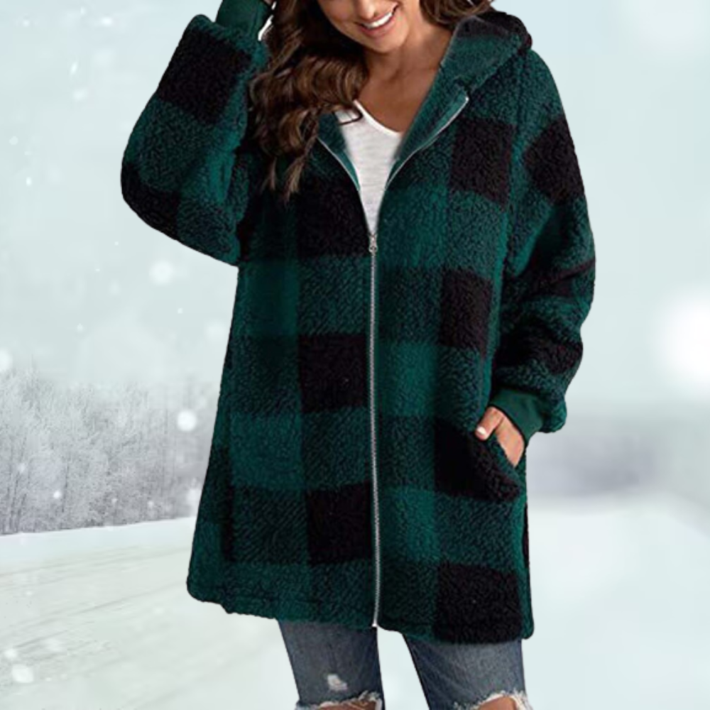 Frau in kariertem Wintermantel, grün-schwarz, mit Kapuze, vor schneebedeckter Landschaft. Modetrend, warme Winterkleidung, Outdoor-Mode.