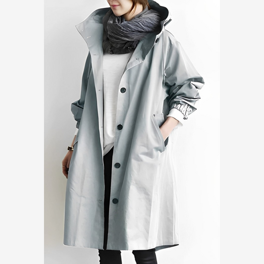 Frau in grauem Regenmantel mit Kapuze und schwarzem Schal. Modischer, wasserdichter Mantel für Damen. Eleganter Herbst- und Winterlook.