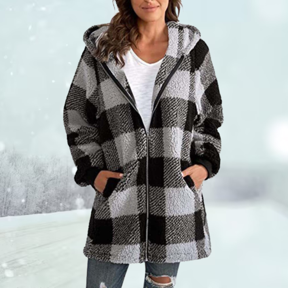 Frau in kariertem Wintermantel mit Kapuze, Schwarz-Weiß-Muster, lässiger Stil, verschneite Landschaft im Hintergrund.