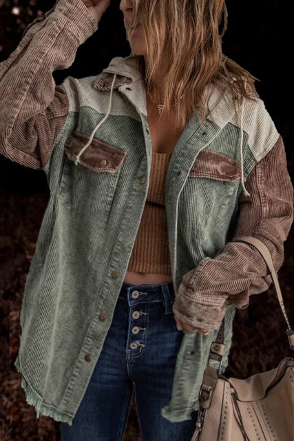 Frau in modischer Cordjacke mit Farbblock-Design in Grün und Braun, kombiniert mit Jeans und Stricktop, hält eine beige Handtasche.