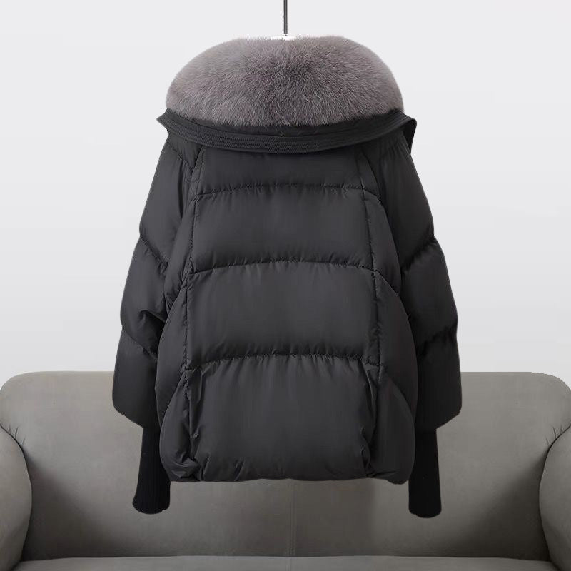 Schwarze Daunenjacke mit grauem Pelzkragen, hängend über einem grauen Sofa. Wintermode, warme Oberbekleidung, stilvolle Damenjacke.