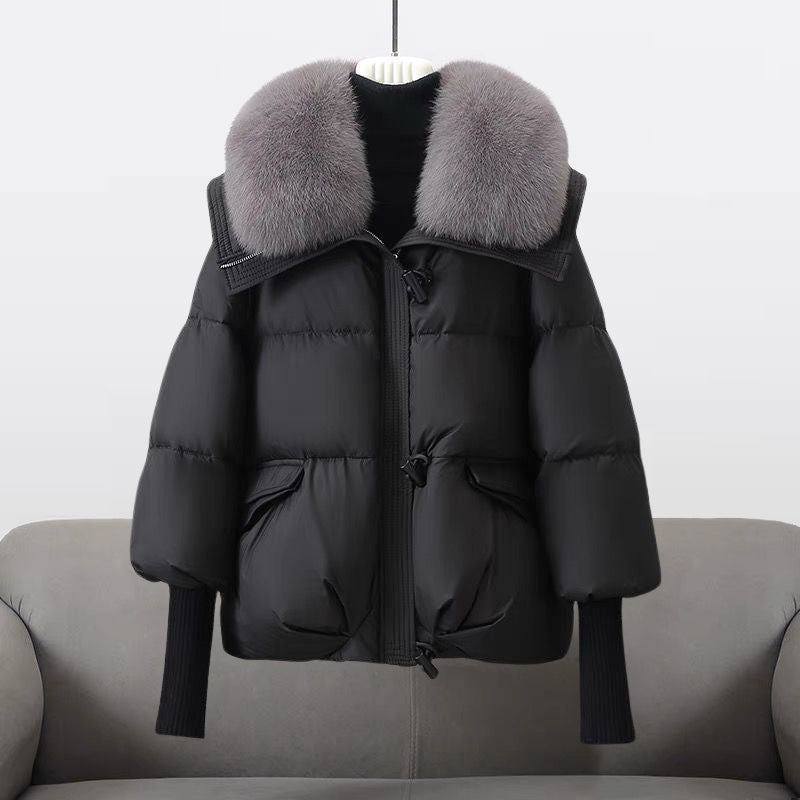 Schwarze Daunenjacke mit grauem Pelzkragen, hängend auf grauem Sofa. Wintermode, warme Oberbekleidung, stilvolle Damenjacke.