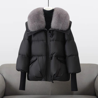 Schwarze Daunenjacke mit grauem Pelzkragen, hängend auf grauem Sofa. Wintermode, warme Oberbekleidung, stilvolle Damenjacke.