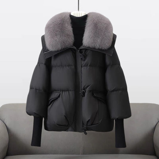 Schwarze Daunenjacke mit grauem Pelzkragen, hängend auf grauem Sofa. Wintermode, warme Oberbekleidung, stilvolle Damenjacke.