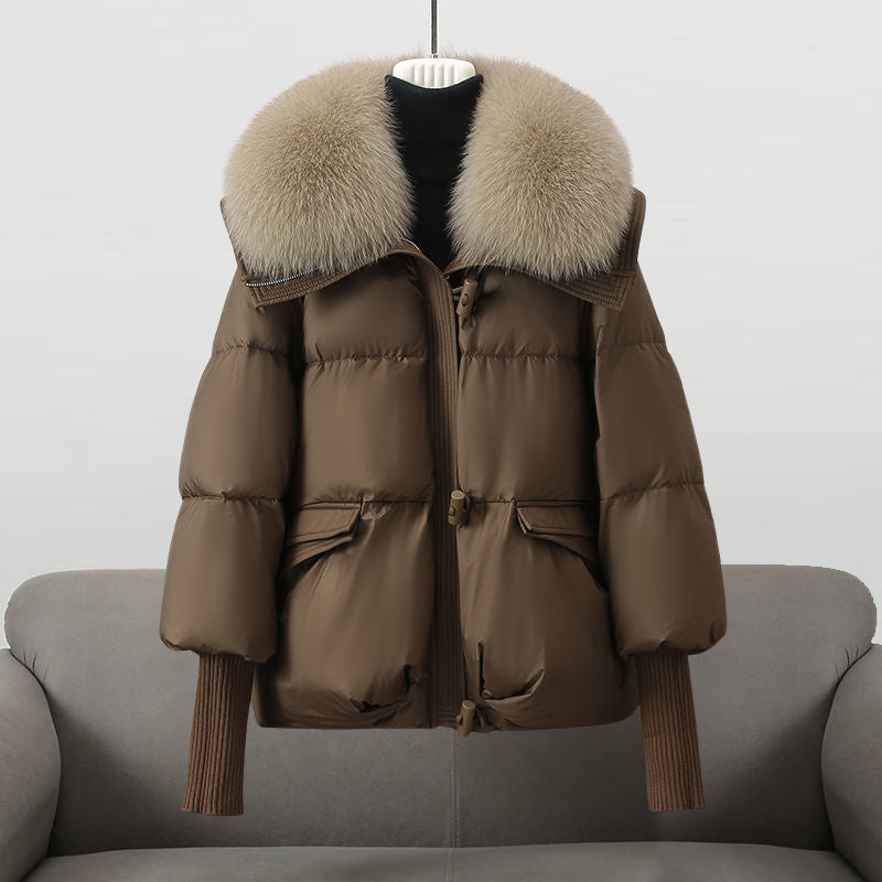 Braune Daunenjacke mit großem Pelzkragen, auf grauem Sofa präsentiert. Wintermode, warme Oberbekleidung, stilvolle Damenjacke.
